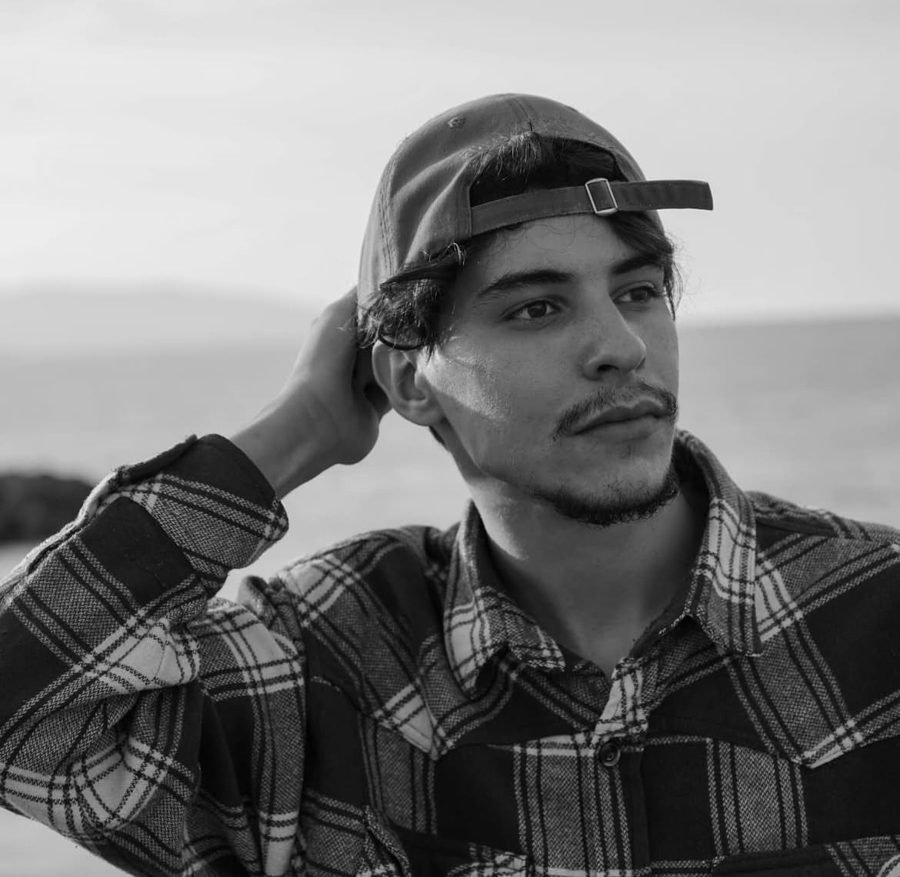 Wael, motion designer, in a cap and plaid shirt by the sea